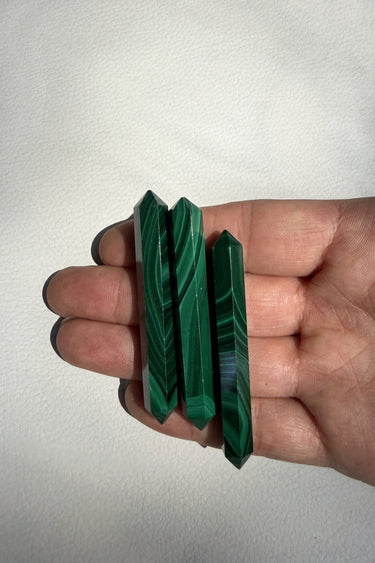 Three polished green malachite crystal points held in a person's hand against a plain off-white background.