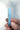 A light blue pointed crystal wand held between fingers against a plain light background.