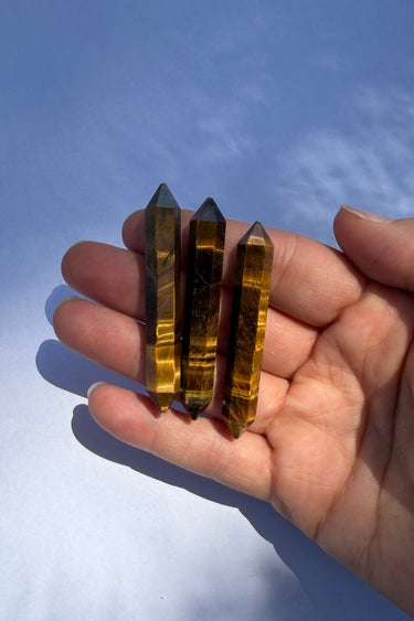 Three Tiger's eye crystal points held in a person's open hand against a blue sky background.