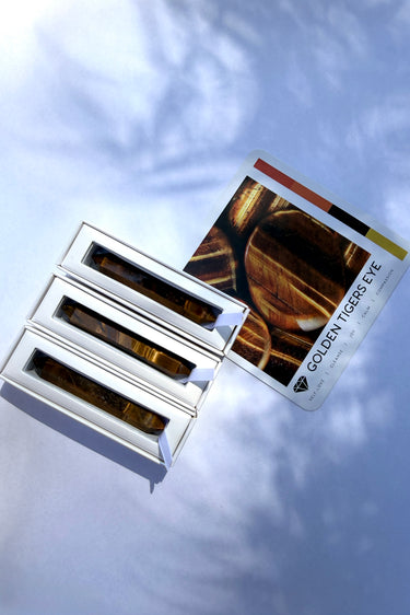 Three Tiger's Eye wands inside their Stoned Crystals packaging with a card explaining the crystal's properties.